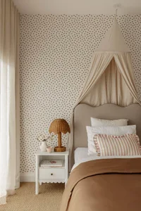 A cozy bedroom featuring a canopy bed with soft fabrics, a side table with a wicker lamp and white pitcher, and heart-pattern