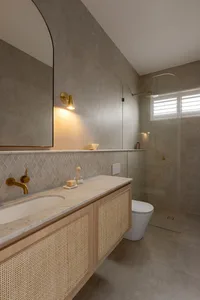 Modern minimalist bathroom with concrete tiles, floating vanity with rattan accents, and gold fixtures.