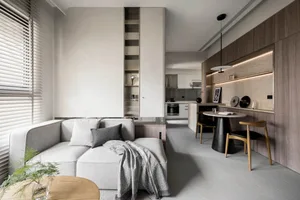 Minimalist living room featuring a light-colored sofa, modern table lamp, and a large window with blinds.