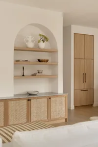 A minimalist white interior design featuring wooden and rattan furniture and shelving.