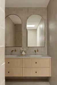 A modern bathroom featuring double sinks, tiled walls, marble countertop, and wooden vanity.