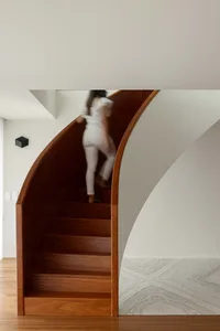 A woman climbing a modern, wooden, curved staircase inside a residential or commercial building.