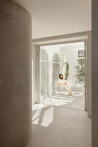 A modern interior with light concrete walls and a woman sitting on a chair in a bright, spacious room.