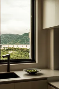 A modern kitchen featuring a minimalist design with concrete finishes, viewed through a window overlooking mountains and a br
