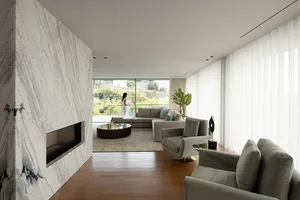 Modern minimalist living room with marble fireplace and large windows overlooking greenery.