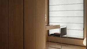 A minimalist study area with a wood and metal desk, a black chair, and a window with horizontal blinds.