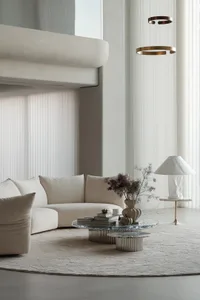 A modern living room featuring a curved sofa upholstered in neutral-toned leather, a round marble side table, and a hanging b