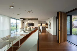 A modern residential interior with wooden floors, featuring a spacious living area with large windows, a kitchen, and an open
