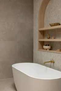 A minimalist bathroom with concrete walls, a white bathtub, and a wooden shelf with decorative items.