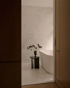 Modern minimalist bathroom featuring a white marble bathtub and a small table with a vase of flowers.