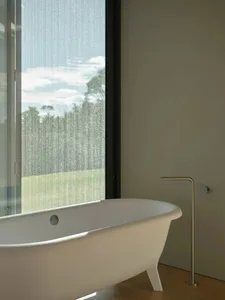 A minimalist white bathtub with a freestanding faucet in a bathroom with a large window showcasing a green landscape.
