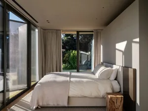 A minimalist bedroom featuring a glass door and white bedding.