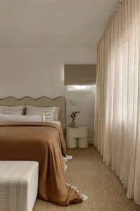 A minimalist bedroom featuring a bed with striped bedding and a woven carpet floor.