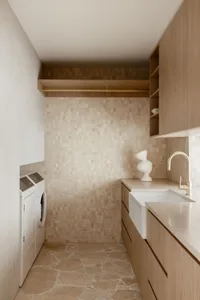 Modern minimalist laundry room with tile flooring and walls, featuring a white sink and integrated cabinetry.