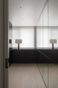 Modern minimalist wardrobe with glass doors and a single table lamp with a white shade and wooden base.