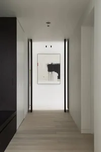 A modern hallway with minimalist black and white decor, featuring abstract art on the wall and dark wooden cabinets.