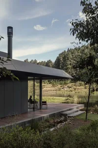 A modern house with a wooden deck and glass walls overlooking a serene lake surrounded by lush greenery, featuring a minimali