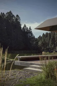 A modern concrete structure on a lakeside, surrounded by natural vegetation and a forested area.