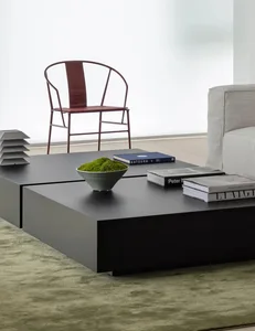 A modern living room featuring a black metal platform coffee table, a grey sofa, a red chair, and a green vase.