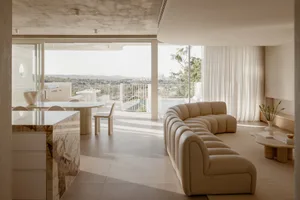 A modern living room featuring a neutral color palette and marble accents, offering a breathtaking outdoor view.
