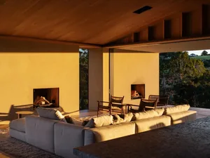 Modern living room featuring a comfortable sofa and two chairs in front of a large window with a view of the trees, illuminat