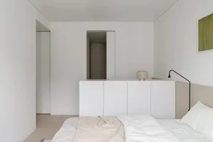 Modern minimalist bedroom with white bed set and wooden floor.