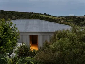 Modern house with corrugated metal siding and a large open doorway with a warm interior light.