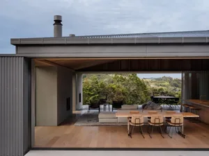 Modern residential interior with wood floors, concrete walls, and glass windows overlooking a natural landscape.