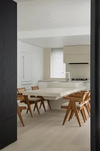 A modern residential kitchen with concrete countertops, white cabinets, and wooden chairs.