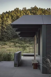 Modern residential porch with concrete roof and walls, surrounded by greenery and trees in the distance.