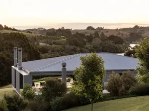 A modern rural house with a metal-clad roof surrounded by greenery and hills.
