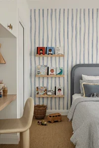 A modern bedroom featuring striped wallpaper, wooden shelves, and a green chair.