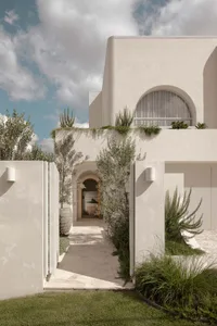 Modern home with white rendered stone exterior, featuring large windows and lush greenery.