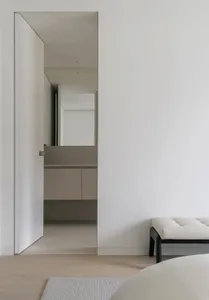 Modern minimalist white bedroom suite with neutral tones, clear glass shower enclosure, white bedding, and sleek black accent