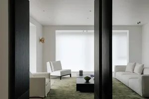 A minimalist living room featuring a sofa and armchairs, with a green rug and a dark coffee table.