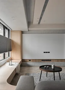 A minimalist living room with a wooden sofa, concrete floor, and a black round table with a vase and teacups.