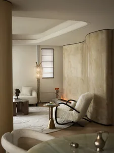 A modern living room with white marble walls and floor, featuring a circular white sofa with colorful cushions and large wind
