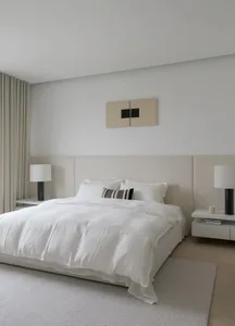 A modern minimalist bedroom with neutral tones, featuring a large bed with white bedding, two side tables with black lamps, a