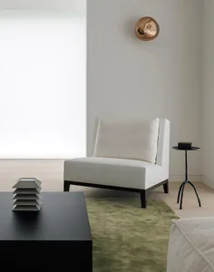 A minimalist living room with a white upholstered sofa on a green rug, a black coffee table, and a metallic wall lamp.