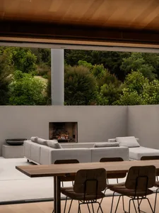 A modern outdoor living room featuring a concrete fireplace, comfortable seating, and a table with chairs.
