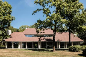 Modern residential building with clay-tiled roof exterior surrounded by green trees and lawn.