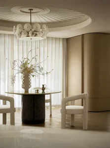 A modern residential dining room featuring a glass table with a vase of flowers, upholstered chairs, and a chandelier.
