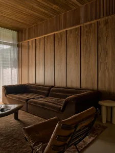 Modern living room with wooden walls and ceiling, featuring a brown plush sofa and a leather accent chair.