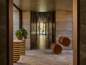 A minimalist interior space with concrete walls, a plant in a large pot, and floating leather stools.