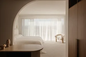 A minimalist bedroom featuring a bed with textured cotton bedding and a textured cotton chair.