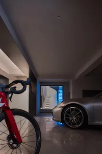 A modern garage interior featuring a sleek, metallic car and a red bicycle against a dark, minimalist background.