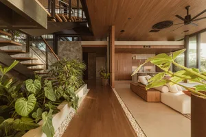 A modern living room with wood elements, including a sofa, plants, and a staircase.