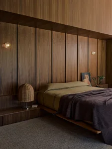 A modern minimalist bedroom featuring wooden paneling, a bed with a wooden platform, and soft lighting.