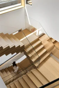 A modern wooden staircase with glass balustrades, viewed from above.