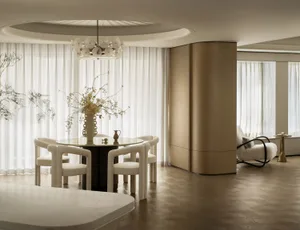 A white dining room with floral decor, including a circular glass table, chairs with white textured fabric, and a vase with f